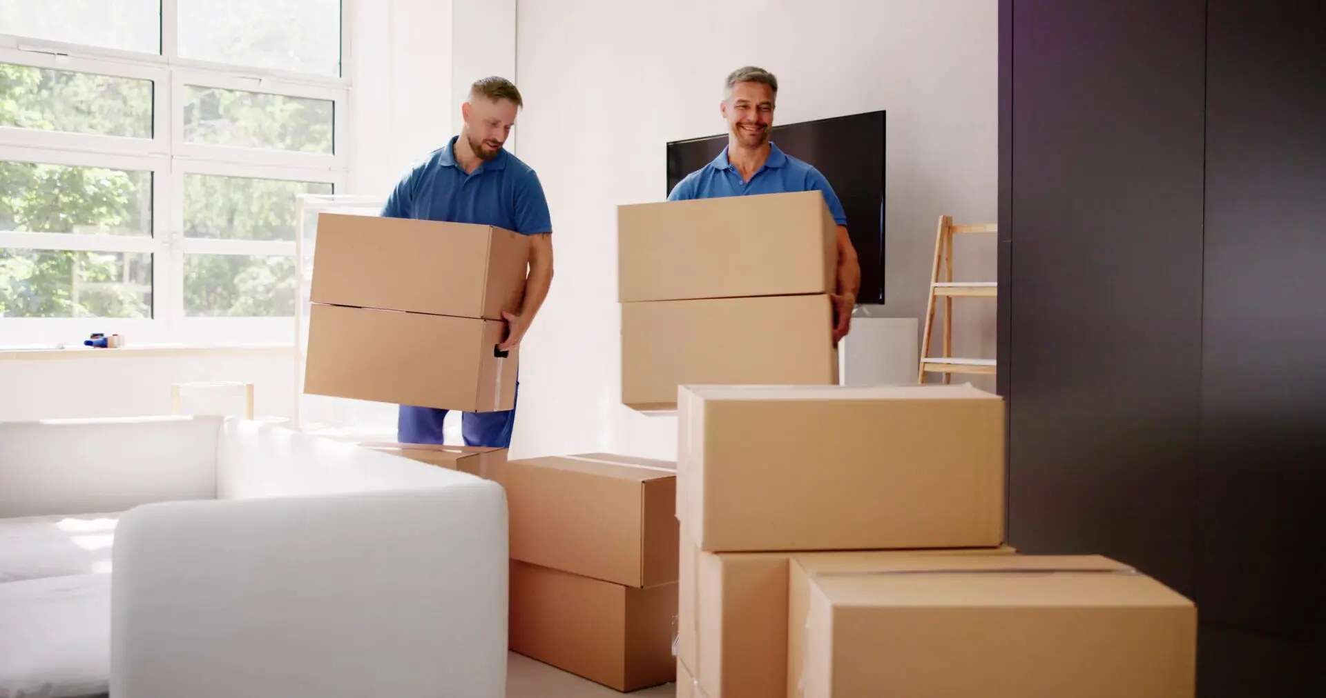 Two movers carrying stacked boxes indoors.