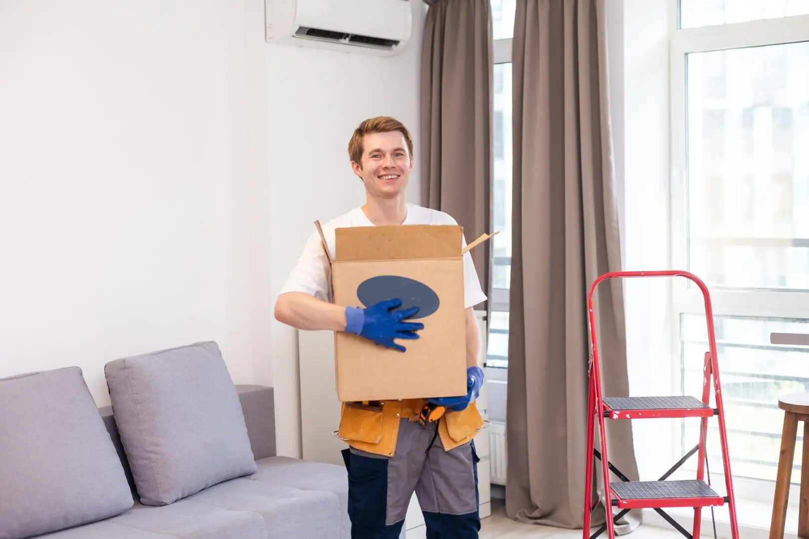 Smiling mover holding a box indoors.