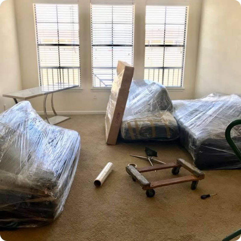 Living room with a couch covered in plastic, a table, a cart, a cardboard box, a hammer